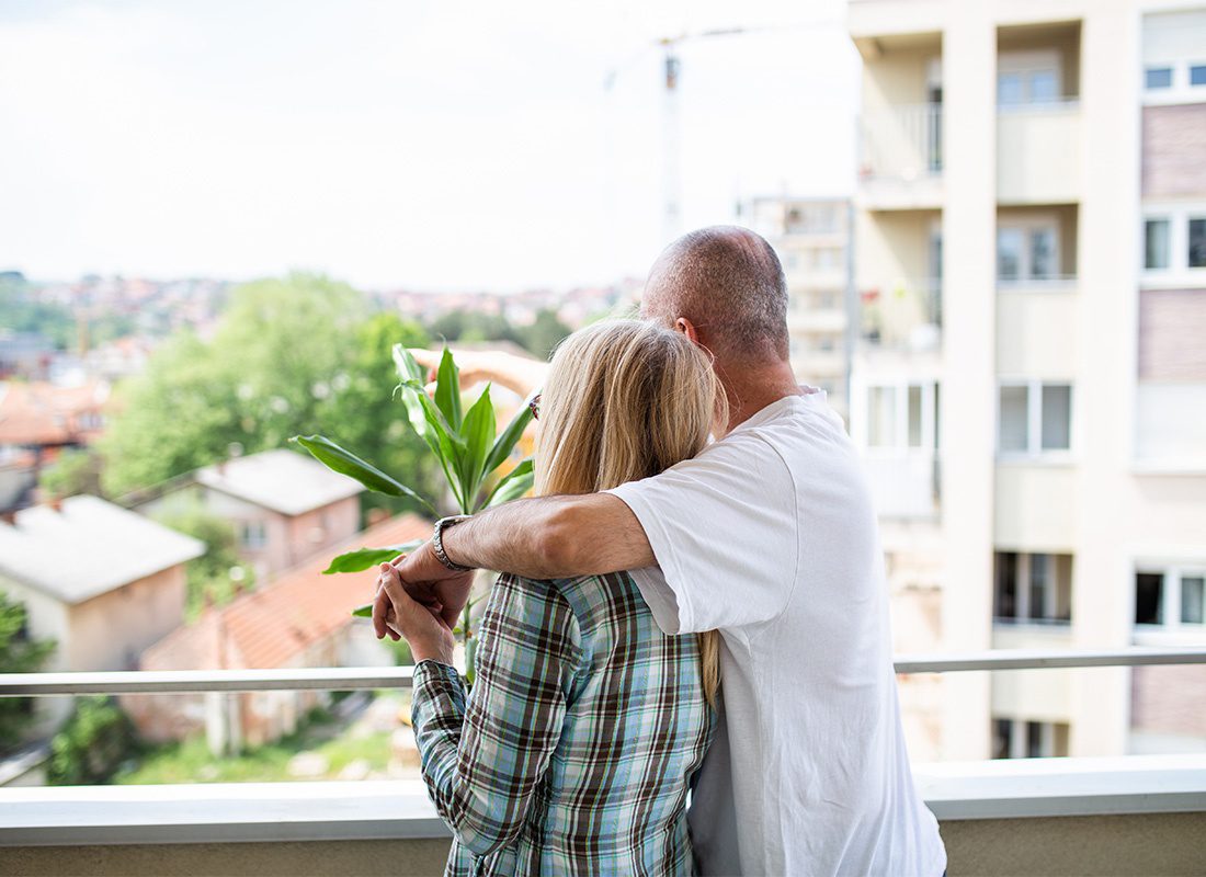 Insurance Solutions - Rear View of an Older Married Couple Standing on the Balcony of Their Apartment Unit Looking at the Views Around Them